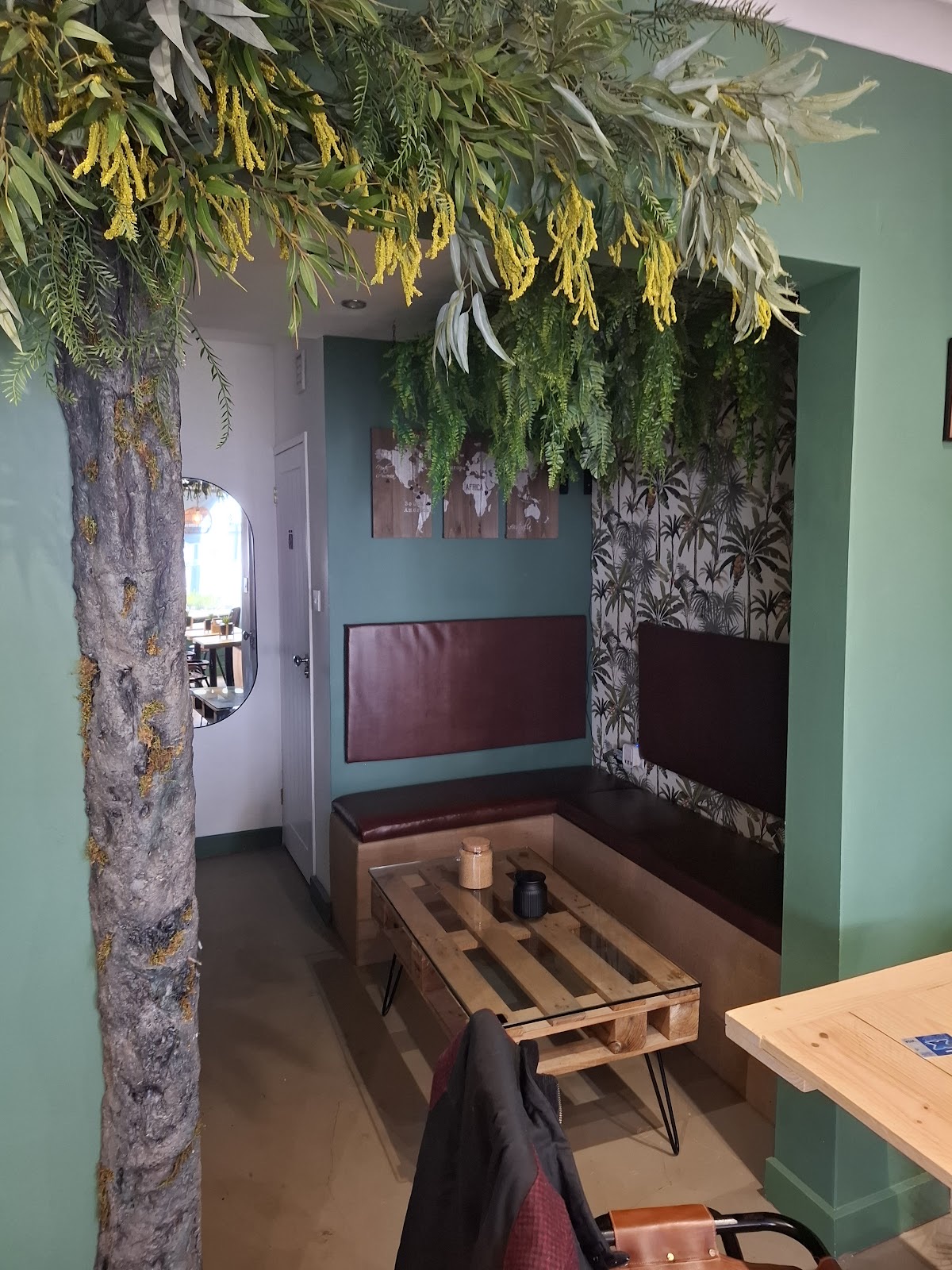 A booth seat under hanging foliage beside a pallet table